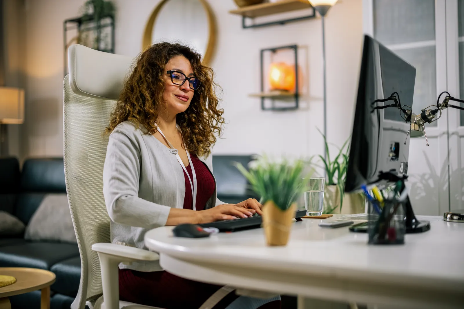 A woman wearing glasses working at a desktop computer in a home office.